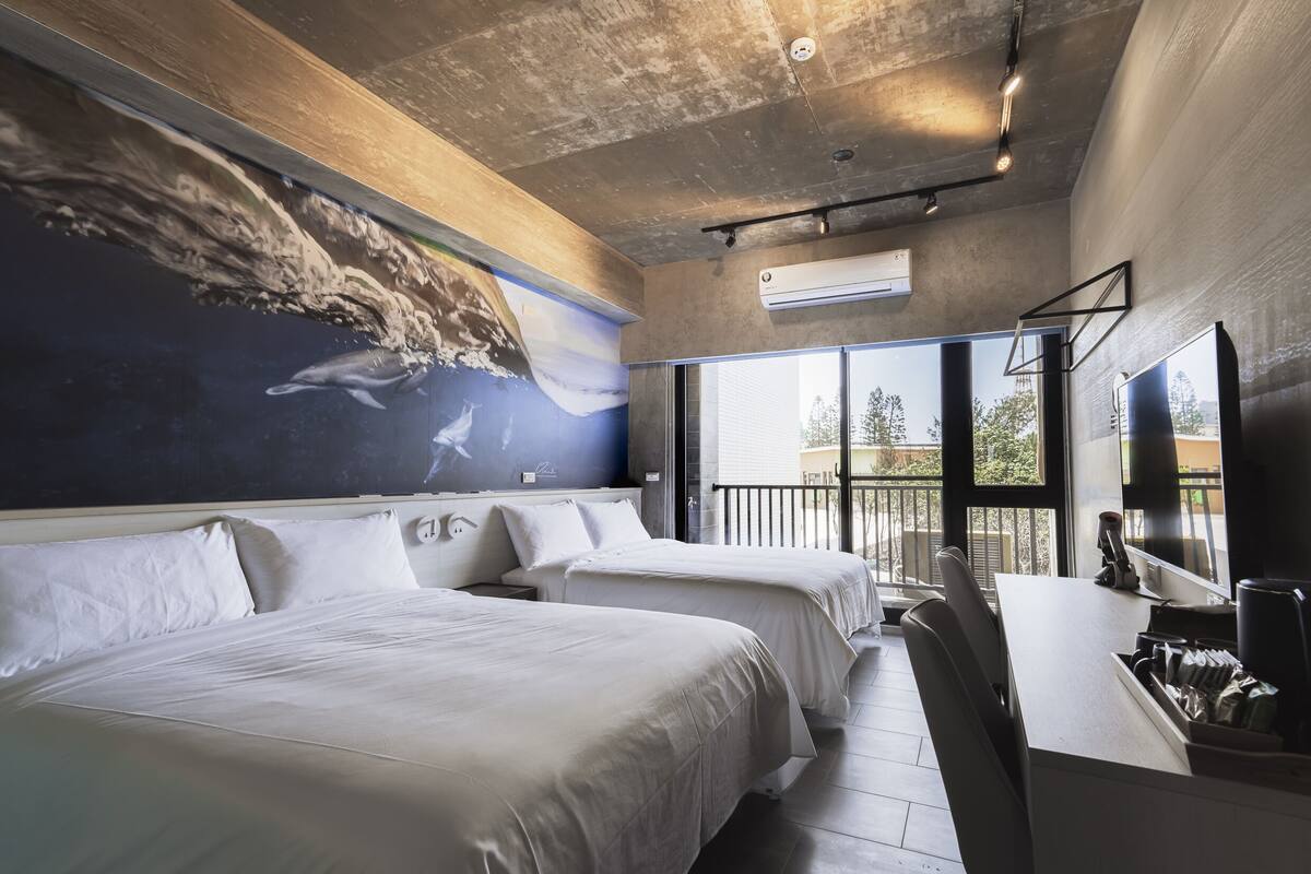 A hotel room with two beds, a large mural of dolphins, a balcony with a view, and a desk with a chair.