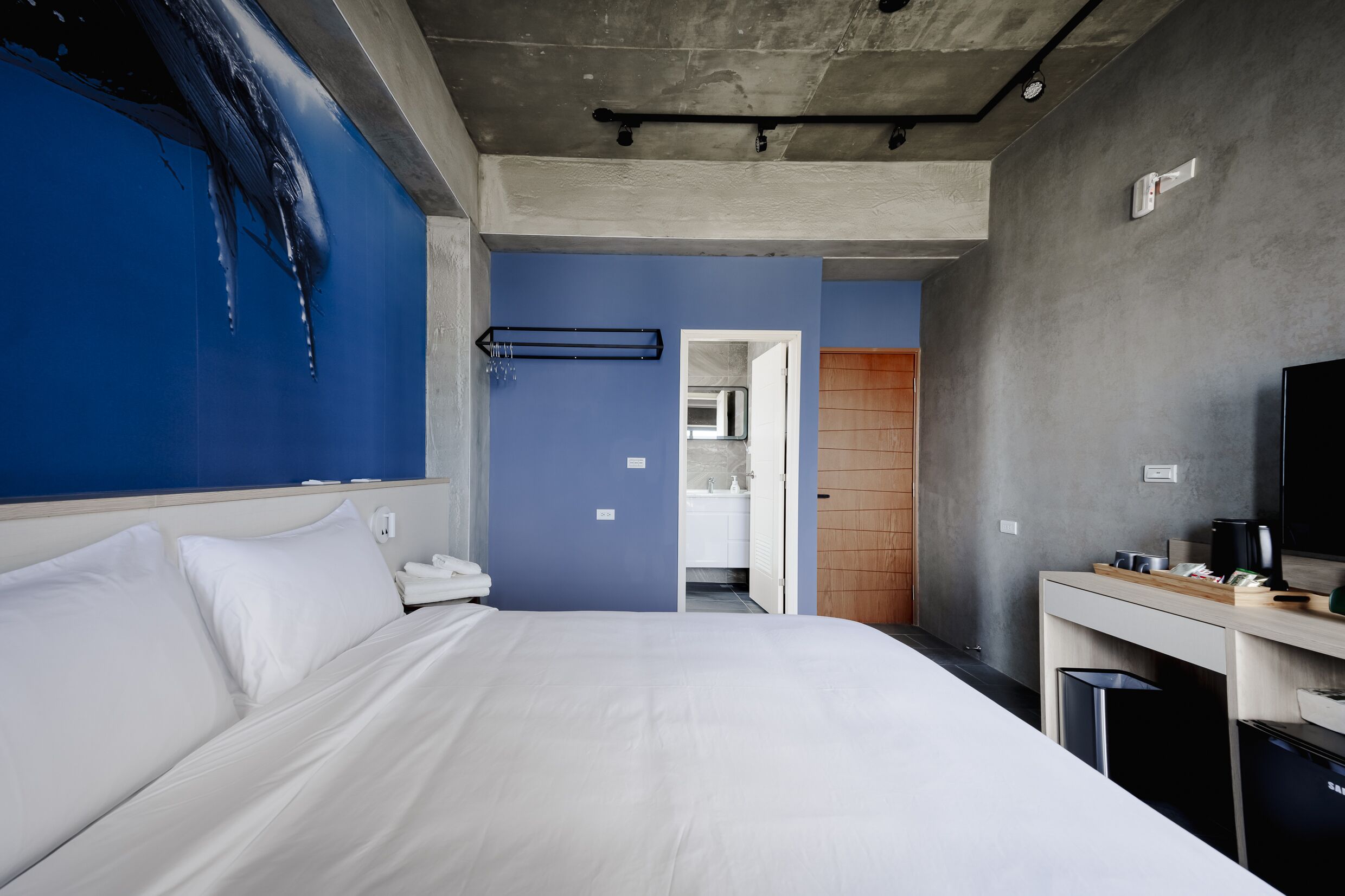 Una camera d'albergo moderna con un letto grande, una televisione, una scrivania e un bagno visibile attraverso una porta aperta.