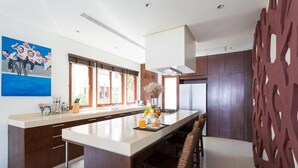A modern kitchen with a large island, wooden cabinets, and a decorative wall piece. - Amatapura Beach Villa 12 (Krabi)