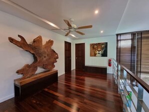 Ein geräumiger Flur mit Holzboden, Deckenventilator, einer großen Holzskulptur und einem Gemälde eines Löwen an der Wand.