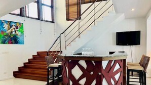 A modern living room with a staircase, a glass-top coffee table, and a flat-screen TV. - Amatapura Beach Villa 12 (Krabi)