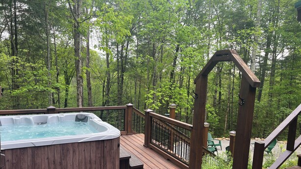 Een hottub op een houten terras, omringd door een bos.