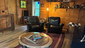 Een gezellig kamer in blokhutstijl met twee leren fauteuils, een houten salontafel, een geweven vloerkleed en een plank met decoratieve objecten.