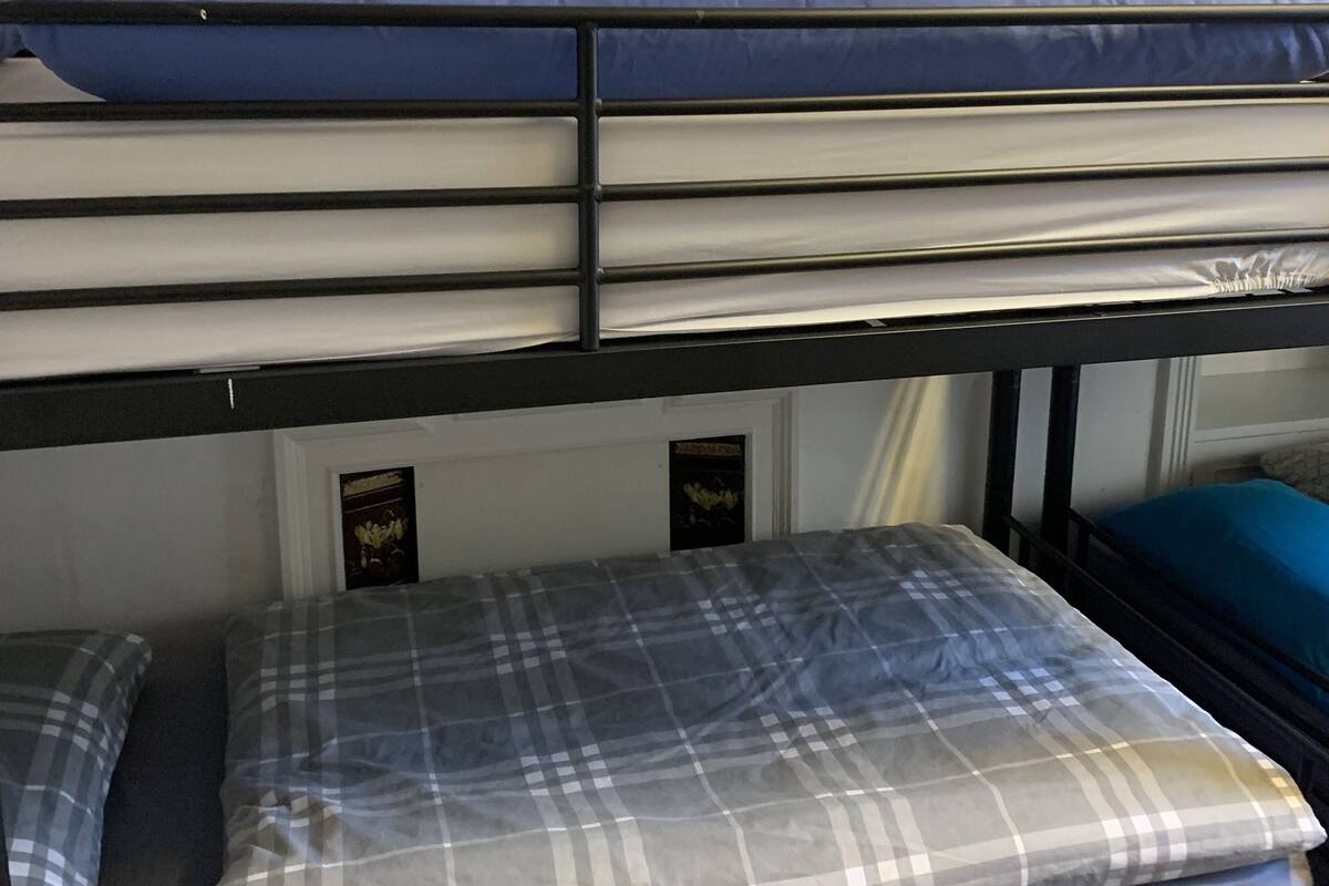 Un lit superposé avec un matelas bleu en haut et un lit inférieur recouvert d’une couverture à carreaux.