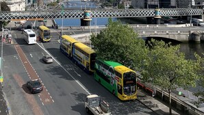 Une rue animée en milieu urbain, avec des autobus, des voitures et un pont enjambant une étendue d’eau.