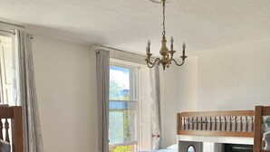 Une pièce avec un lit superposé, une table ronde entourée de quatre chaises, un lustre et une cheminée.