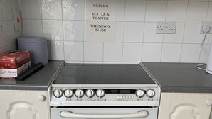 Une cuisine avec des meubles blancs, un four à deux cavités et un plan de travail sur lequel se trouvent une bouilloire et un grille-pain.