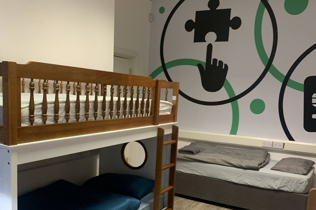 Une chambre avec un lit superposé, une échelle, un lit inférieur et un mur décoré d’œuvres d’art abstraites.