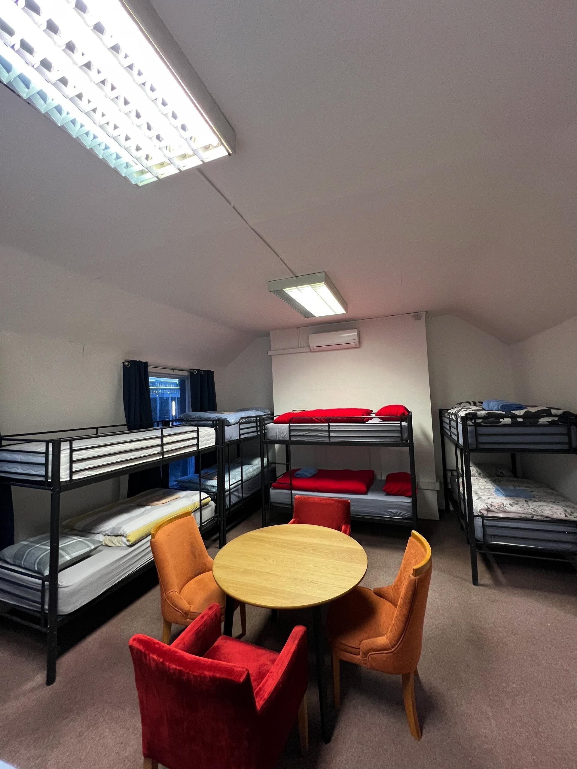 A dormitory room with bunk beds, a round table, and two chairs.