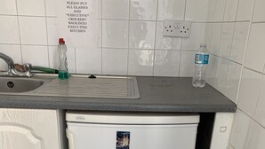 Une cuisine équipée d’un évier, d’une bouteille de liquide vaisselle et d’une bouteille d’eau. Un panneau est affiché au mur, indiquant qu’il faut remettre les verres et la vaisselle dans la cuisine réservée aux cadres.