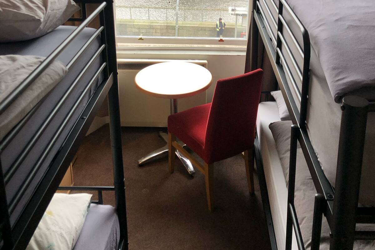 Une chambre d’hôtel avec des lits superposés, une petite table ronde, une chaise rouge et une vue sur le paysage urbain par la fenêtre.