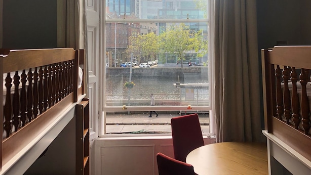 Une pièce dotée d’une grande fenêtre donnant sur un paysage urbain, d’une petite table ronde et d’une seule chaise rouge.
