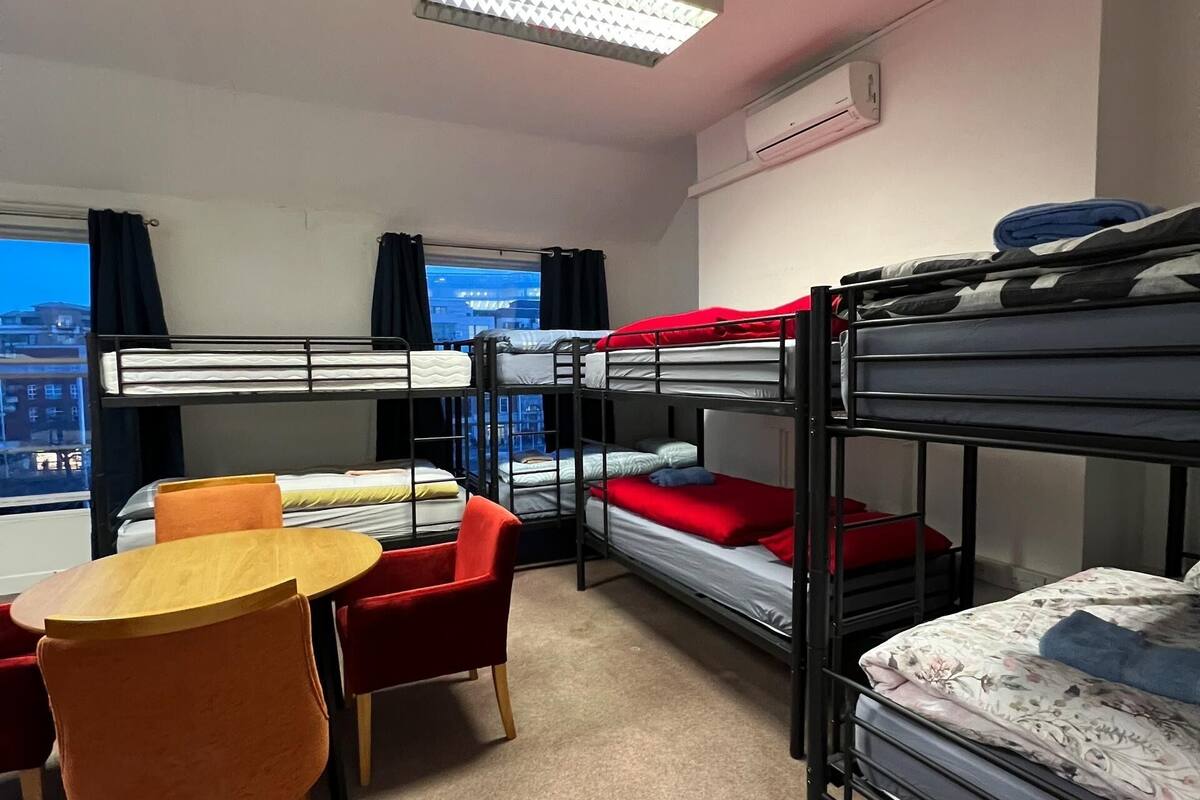 Une chambre de dortoir avec des lits superposés, une table ronde en bois et des chaises rouges.