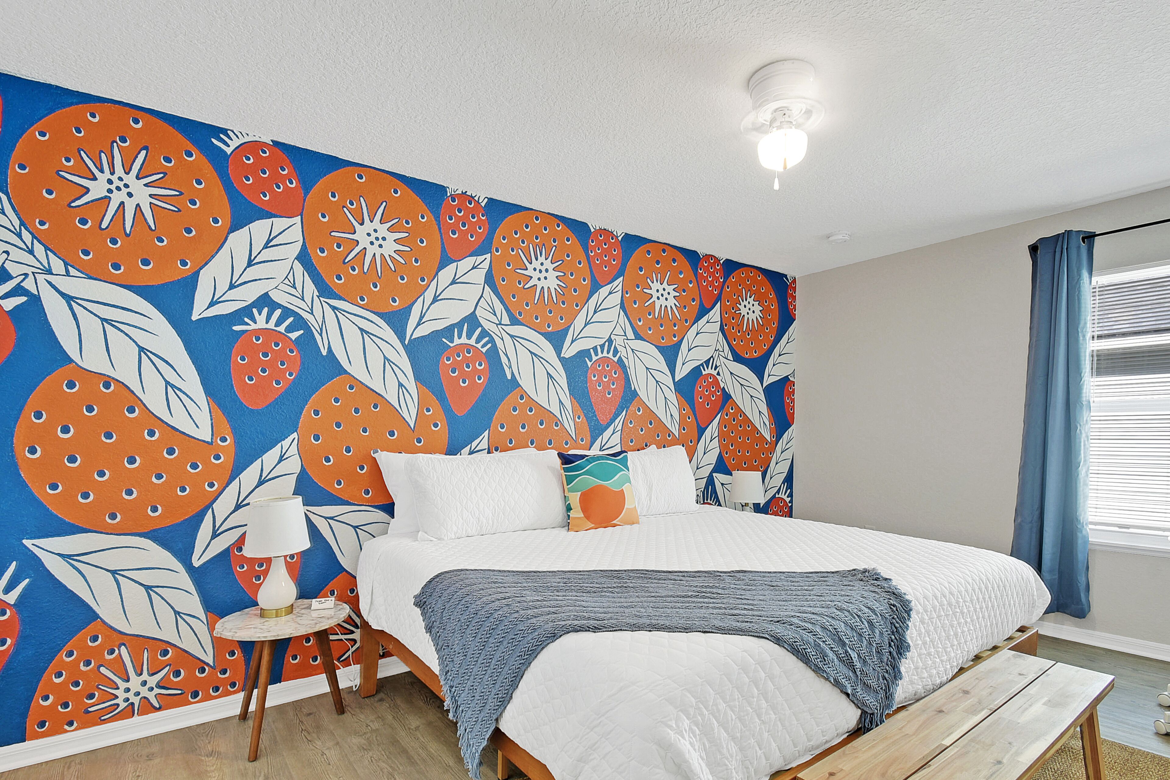 A bedroom with a large bed, a bedside table with a lamp, a wooden bench, and a wall mural.