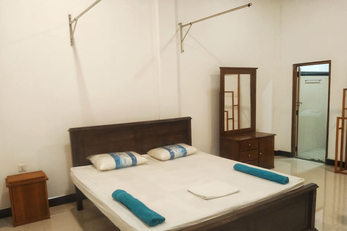 A neatly made bed with pillows and a rolled towel, a wooden nightstand, a dresser, and a mirror.