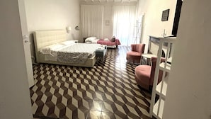 A hotel room with a checkered floor, a bed with a white headboard, a pink armchair, a small table, and a mirror on the wall. - Loft with private bathroom (Arezzo)