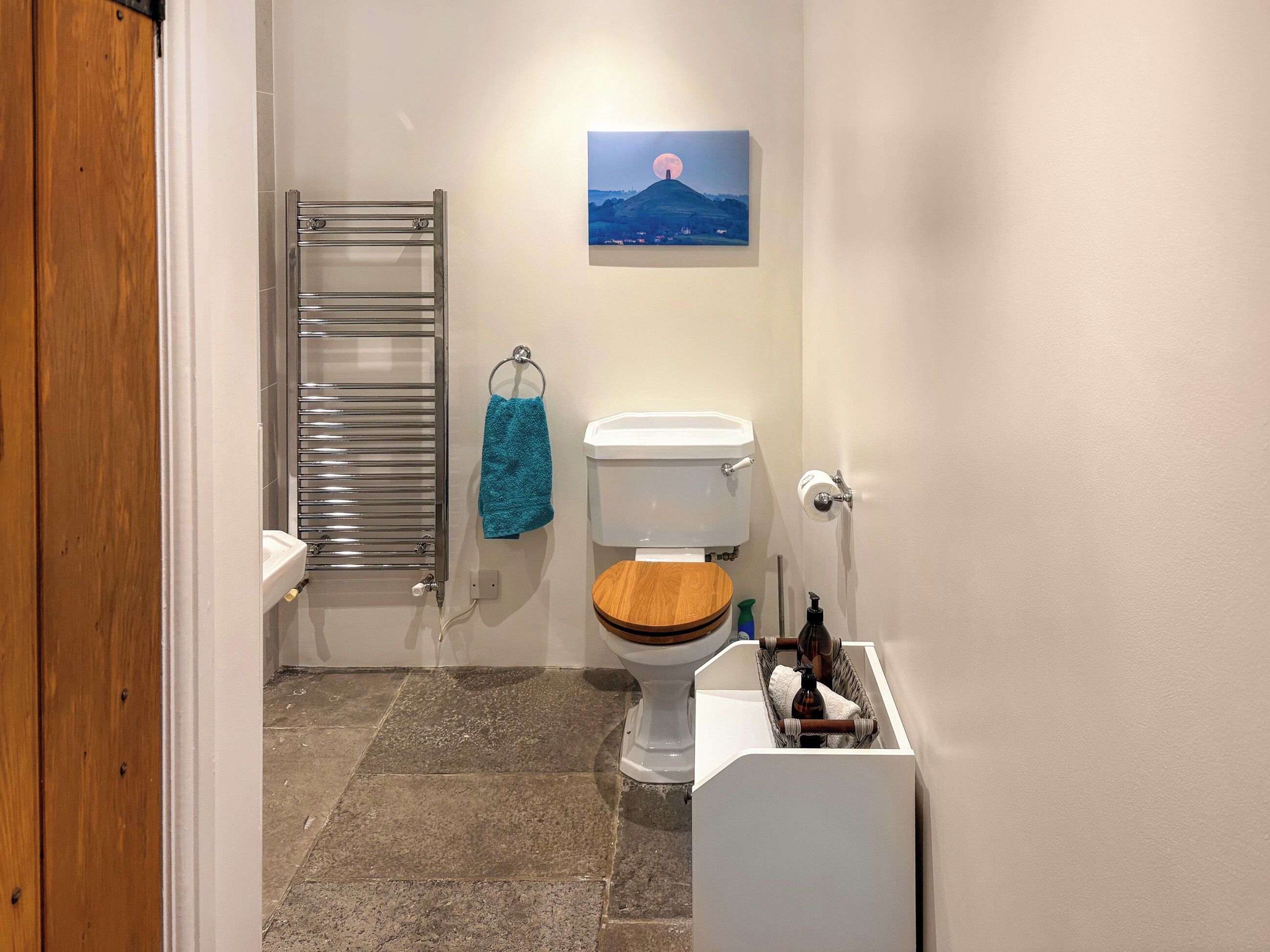 Ein Badezimmer mit Toilette, Handtuchhalter, einem Metall-Handtuchhalter, Holzboden und einem Bild an der Wand.