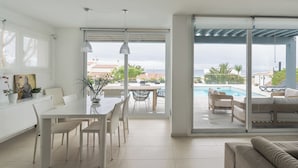 A modern living room with a dining area, a pool, and a view of the sea. - V196| Villa Brisas - Four Bedroom Villa, Sleeps 8 (Torre Soli Nou)