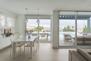 A modern living room with a dining area, a pool, and a view of the sea.
