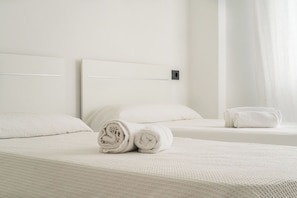 A hotel room with two beds, each with white linens and pillows, and a small bedside table.
