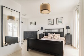A bedroom with a bed, two bedside tables, a dresser, a large mirror, and two framed pictures on the wall.