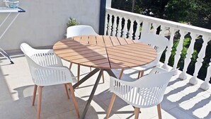 Een ronde houten tafel met vier witte stoelen op een balkon.