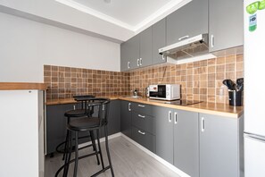 A modern kitchen with grey cabinets, a wooden countertop, and a built-in microwave.