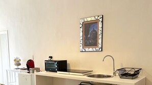 Eine kleine Küche mit weißem Arbeitsplatz, Spüle, kleinem Kühlschrank und einem Metallregal mit Geschirr.
