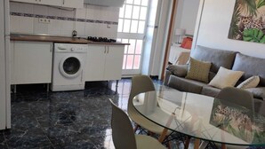 A compact kitchen with a washing machine, a dining area with a glass table, and a sofa with cushions. - Ático en la Costa del sol a 15 Minutos de la Playa .en Tercera Planta sin Ascens (Arenas)