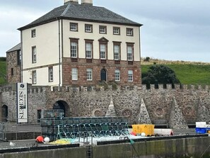 A large, two-story building with a stone wall and a flag reading "DISCOVER SECRETS". - Seaside Lodge Retreat in Eyemouth (Eyemouth)
