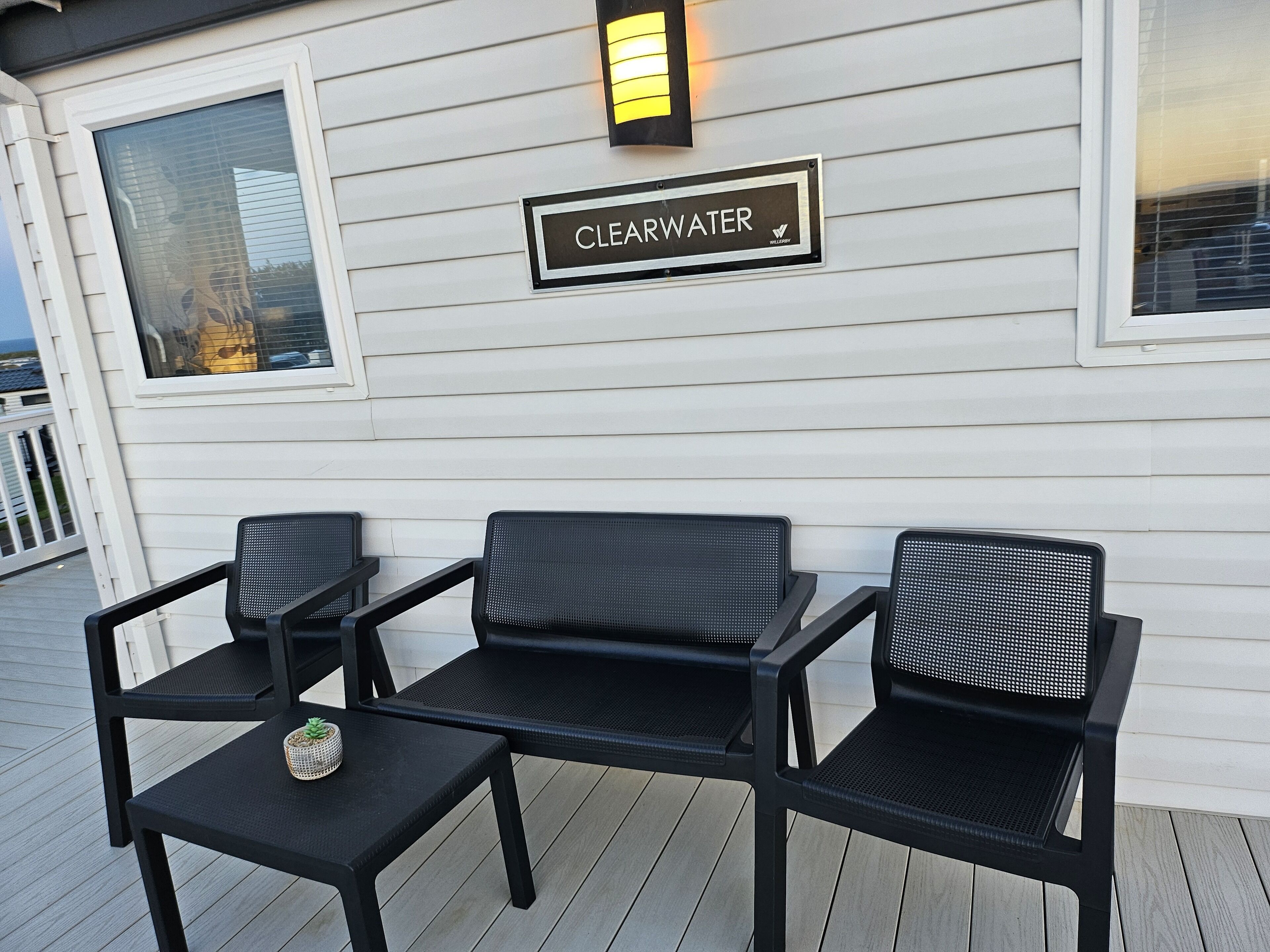 A deck with three black chairs and a small table, a 'CLEARWATER' sign, and a window with blinds.