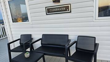 A deck with three black chairs and a small table, a 'CLEARWATER' sign, and a window with blinds.