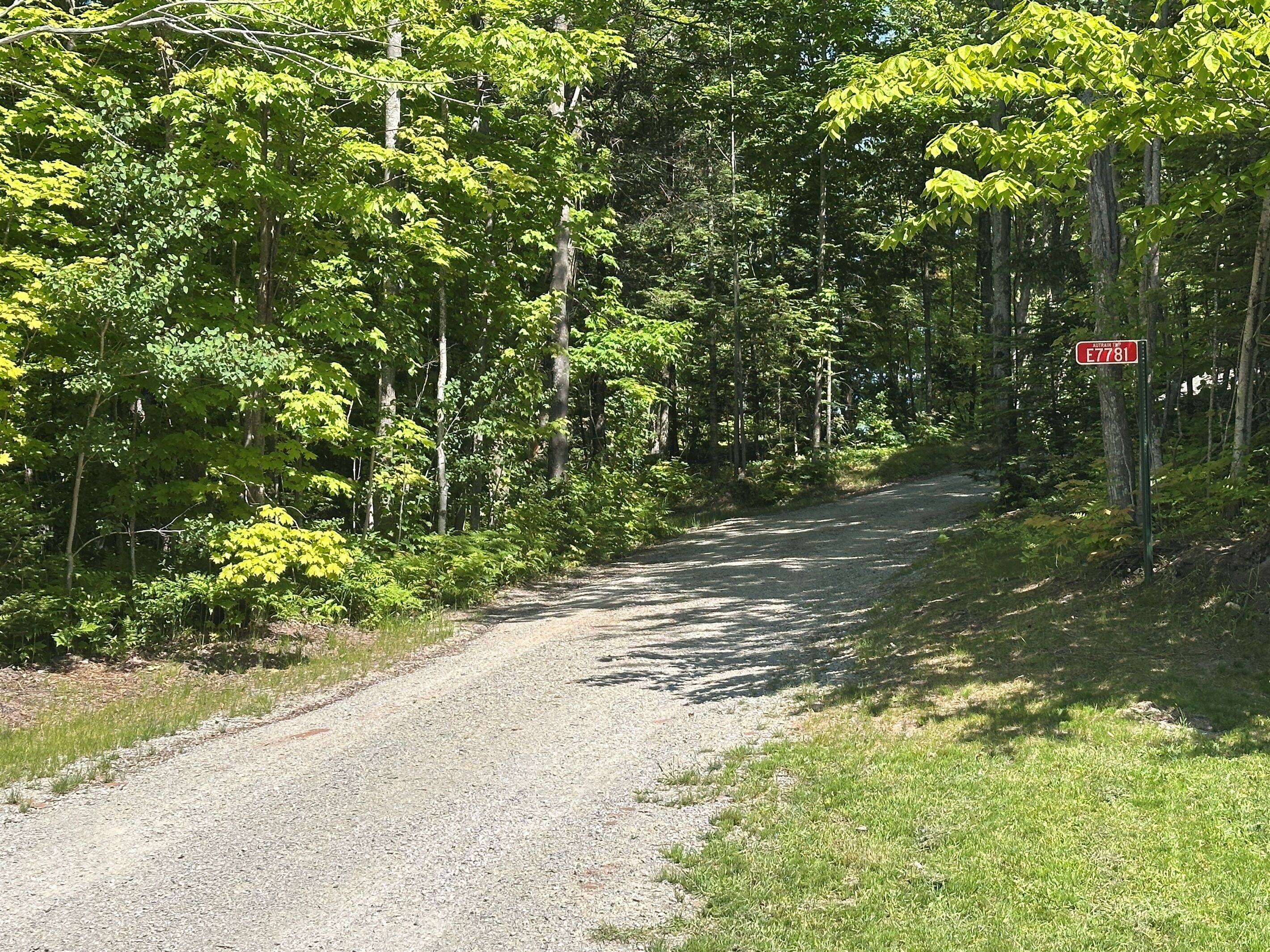 Un chemin de gravier bordé d’une végétation luxuriante et un panneau indiquant « E 7781 ».