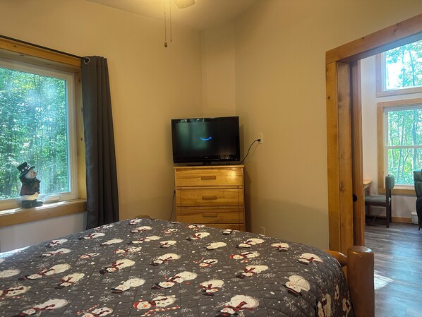 Une chambre à coucher avec un lit, un téléviseur posé sur une commode en bois et une fenêtre avec des rideaux.