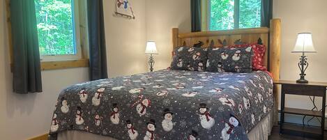 A bedroom with a bed, two bedside lamps, a window with curtains, and a wall decoration.