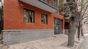 A red brick building with a tiled sidewalk, a tree, and a door. - The Tbilisi Pod (Tbilisi)