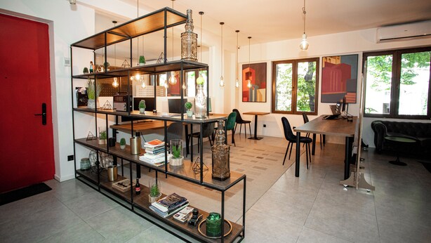 A modern interior with a red door, a multi-tiered glass and metal shelving unit, a dining area with a table and chairs, and large windows allowing natural light. - The Tbilisi Pod (Tbilisi)