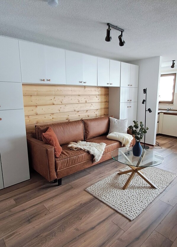 A modern living room with a brown leather sofa, a glass coffee table, and a wooden headboard.