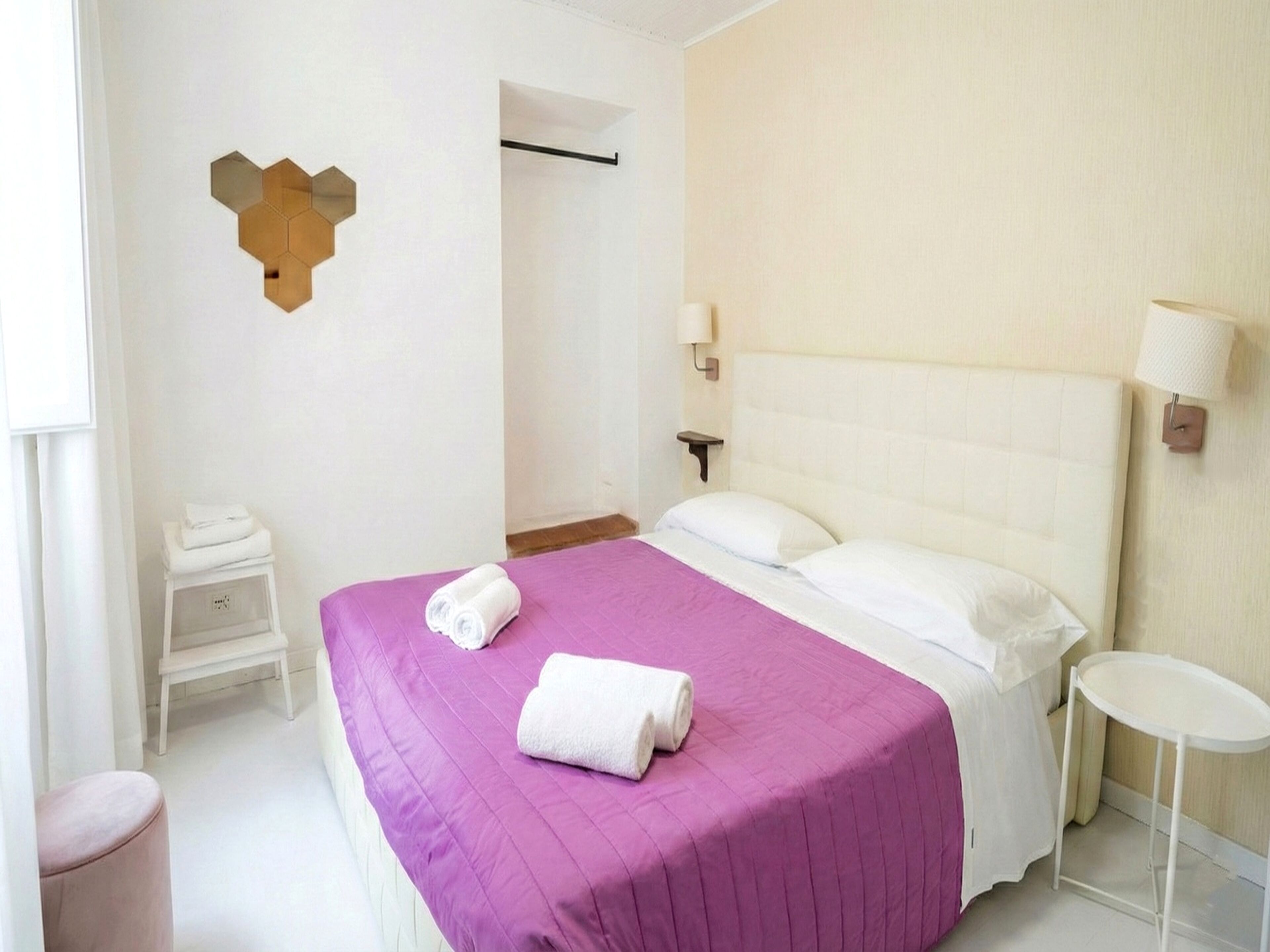 A hotel room with a bed, two bedside lamps, a small table, and a wall-mounted light fixture.