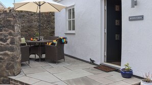 Une terrasse avec une table et des chaises, un mur en pierre et une porte avec une enseigne.