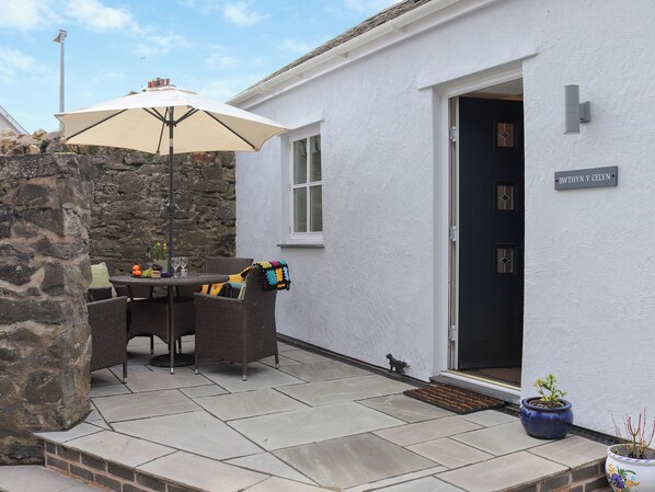 A patio with a table and chairs, a stone wall, and a door with a sign.
