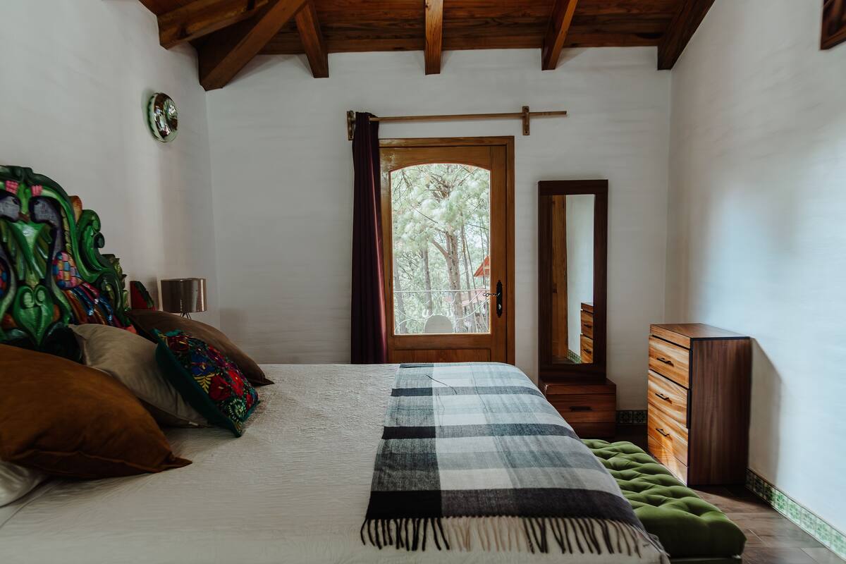 Een slaapkamer met een bed, een dressoir, een spiegel en een raam met gordijnen.