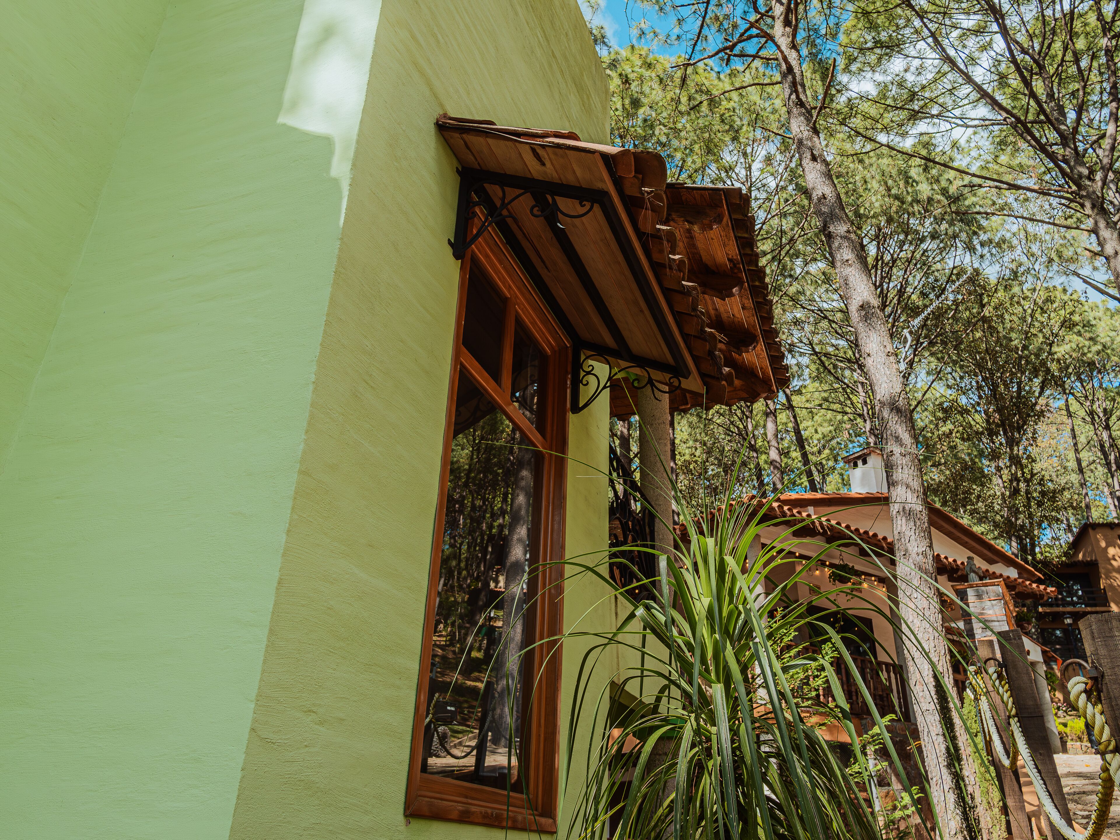 Un edificio con fachada verde, marco de ventana de madera y pérgola de madera.