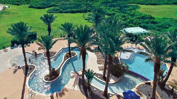 Een resort met een groot zwembad, palmbomen en uitzicht op de oceaan.