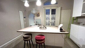 A kitchen with a central island, two stools, a sink, and overhead lighting. - Junior Suite Deluxe per Due, Corso Italia 114 (Arezzo)