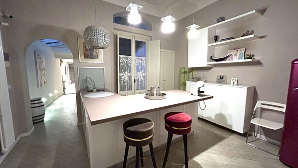 A modern kitchen with a central island, bar stools, a refrigerator, and a dining area. - Junior Suite Deluxe per Due, Corso Italia 114 (Arezzo)