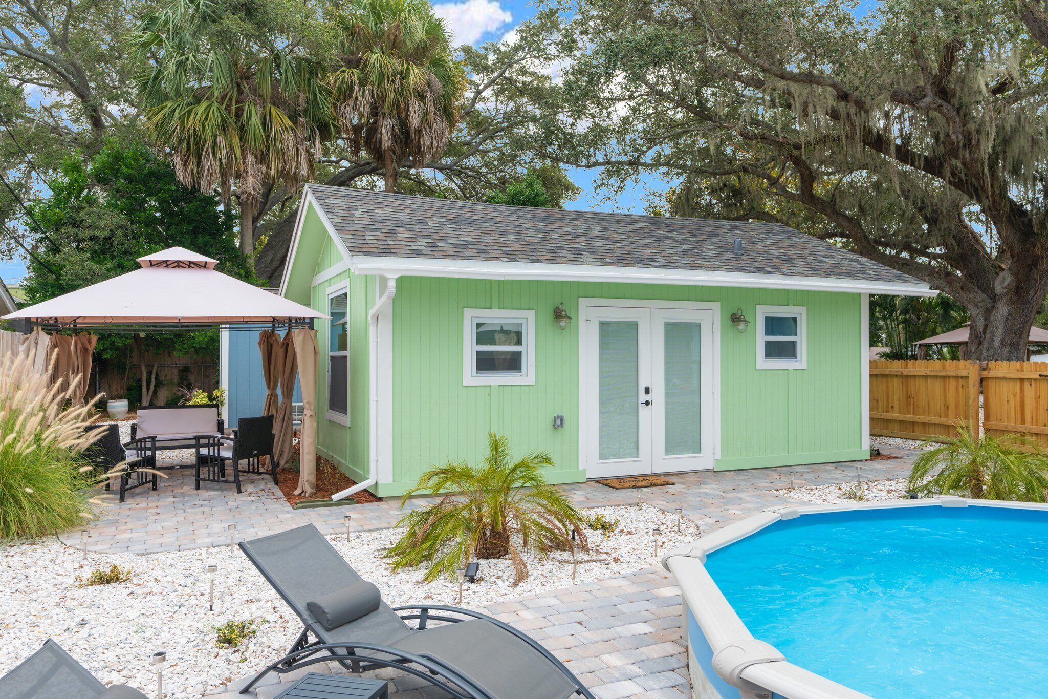 A small green house with a pool, patio furniture, and a covered seating area.