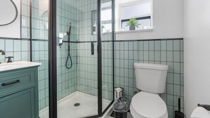 A bathroom with a glass-enclosed shower, a white toilet, and a sink with a blue cabinet. - Sunset Bungalows Lil' Green: Heated Pool, Near Beach & DT, Fenced (Clearwater)