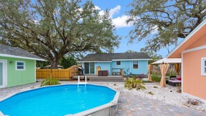 A backyard with a swimming pool, a wooden deck, and a house with a blue exterior. - Sunset Bungalows Lil' Green: Heated Pool, Near Beach & DT, Fenced (Clearwater)