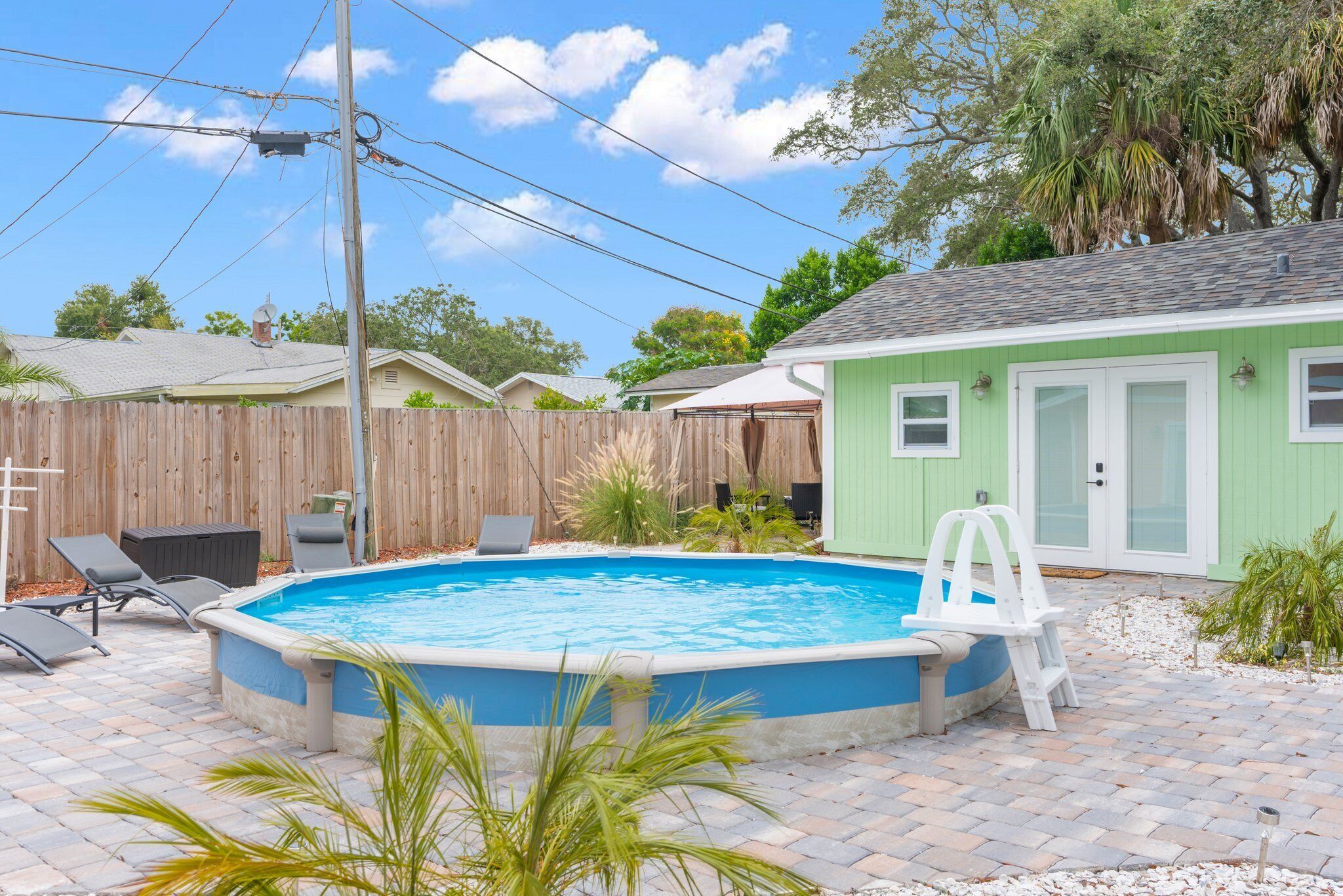 Un patio trasero con piscina, cerca de madera y una casa verde.